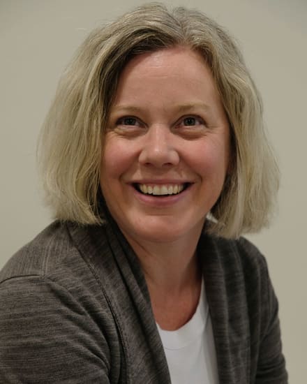 Kristina Dixon, smiling, in a grey cardigan against a plain wall.