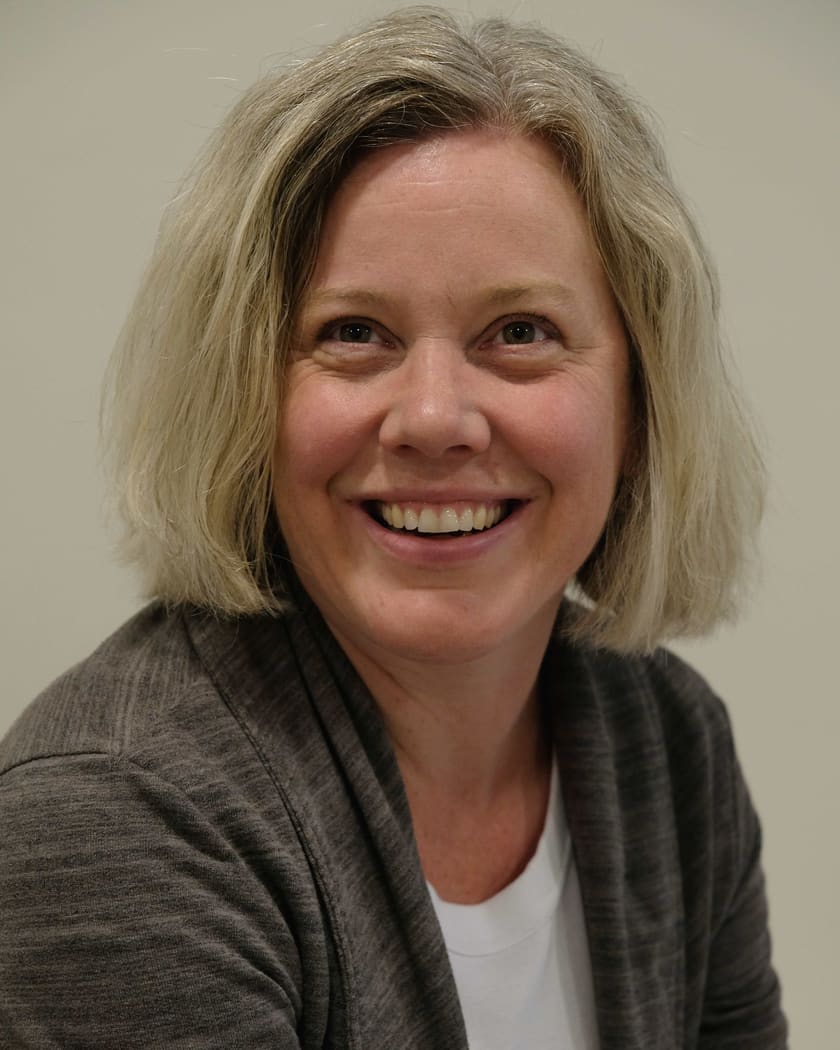 Kristina Dixon, smiling, in a grey cardigan against a plain wall.